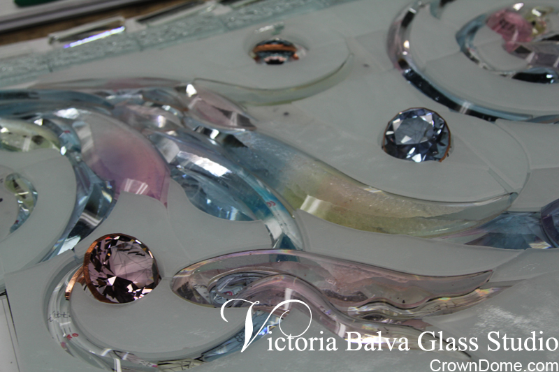 Hand bevelled colored glass laid with water jet cut parts before assembling